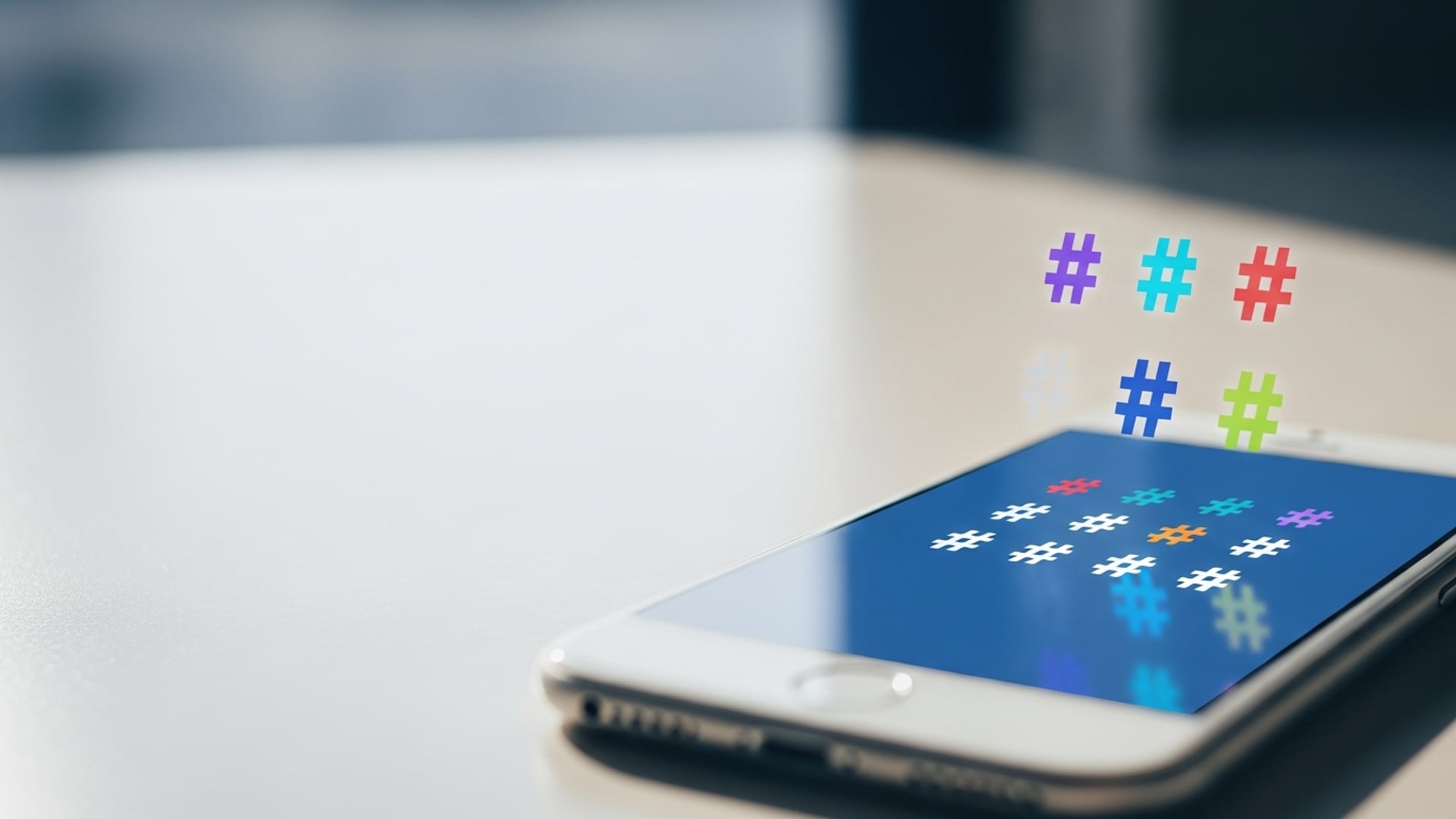 A smartphone resting on a desk with colorful 3D hashtag icons floating above the screen display.